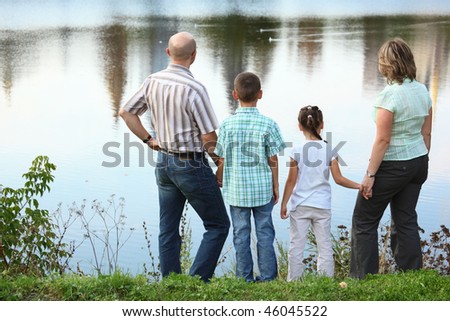family with two children in early fall park near pond. they are looking at water.