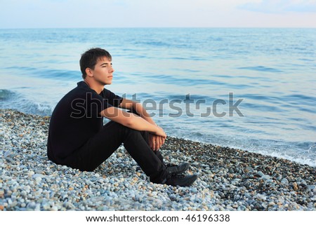 sitting teenager boy on stone seacoast, Looking afar