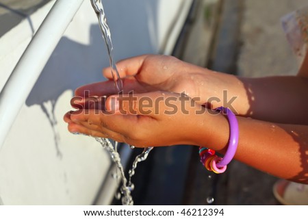 washing of hands of little girl by water from pipe in street