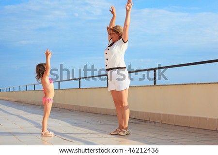 elderly woman and  little girl do morning exercises on veranda near seacoast, lifted hands upwards
