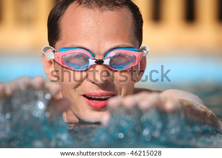 young man in waters sport goggles swimming in pool, extended hands forward