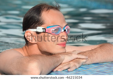 young man in waters sport goggles swimming in pool, near ledge