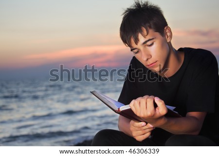teenager boy reads book sitting on beach in evening