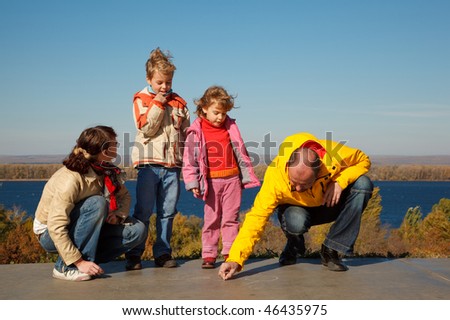 Family from four persons walks in solar autumn day. Parents draw chalk on asphalt.
