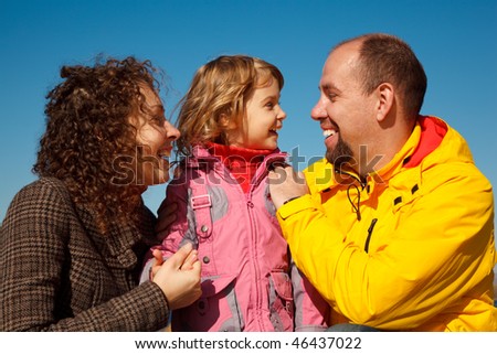 Portrait of happy family against blue sky. Little girl with mum and daddy, in bright autumn day.