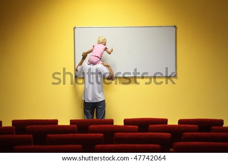 father and little girl in empty presentation hall. little girl is sitting on a father\'s neck. chair in out of focus.