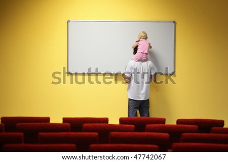 little girl is sitting on father\'s neck and drawing on a board. chair in out of focus.