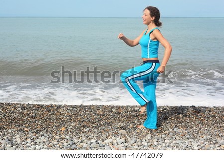 smiling woman wearing sporty clothes is making exercise on sea coast