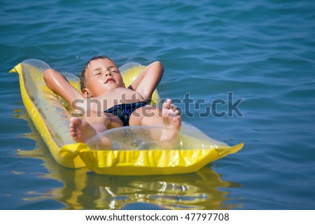 boy in dark blue swimming trunks relaxing on an inflatable mattress in sea