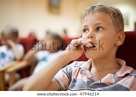 boy sitting in cinema armchair, holding fingers near mouth