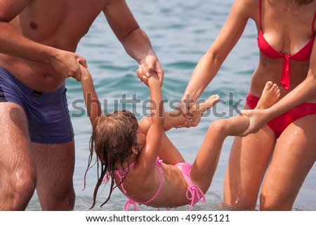 young family bathes in sea. wet happy daddy and mum play with daughter standing in water
