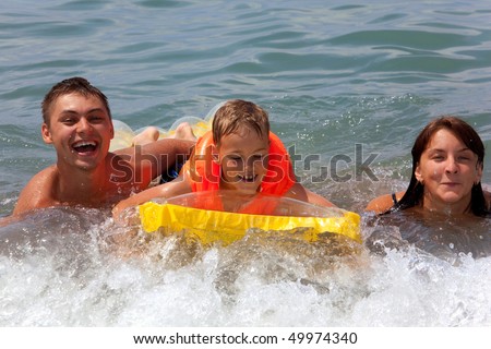 young family with yellow mattress bathes in sea. happy mum daddy and son play in water