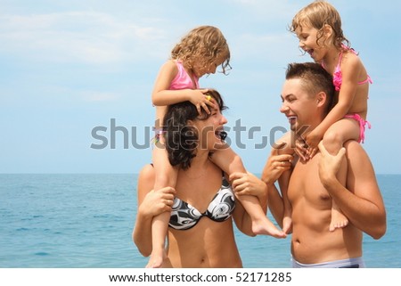 mother and father near water with two little girls sitting on their necks. woman looking at man and man looking at woman.