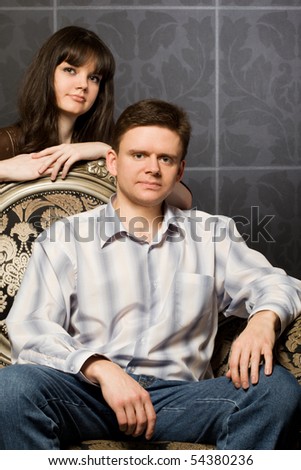 beautiful woman and young man sitting in magnificent ancient armchair against wall with pattern, close up