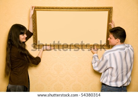 young beautiful woman and smiling man hang up on wall picture in frame, looking at picture