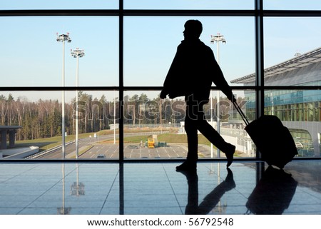 silhouette of man with luggage walking left near window in airport focus on street