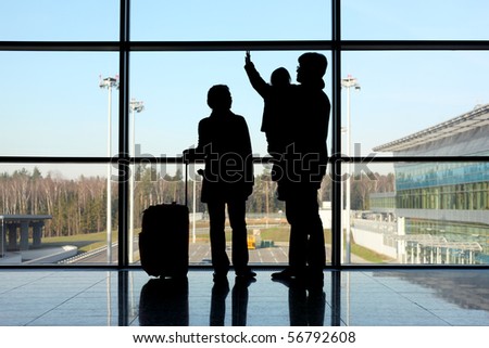 silhouette of young family with luggage standing near window in airport