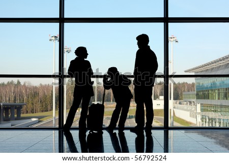 silhouette of mother, father and son with luggage standing near window in airport