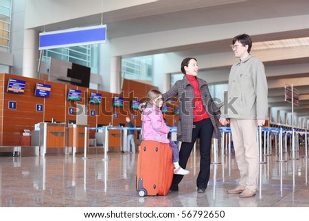 young family with red suitcase standing in airport hall