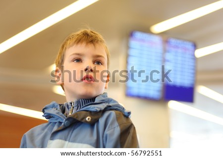 portrait of little boy in airport looking into the distance blue screens on background