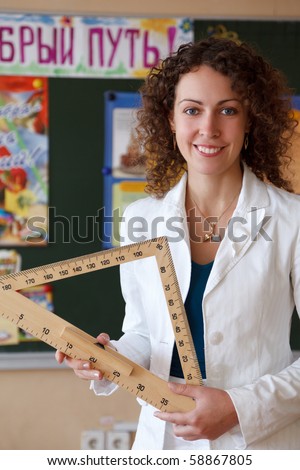 Portrait of schoolteacher in a white blouse in school. Girl with ruler in his hand standing at blackboard. Looks into camera. Vertical format.