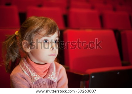 little girl sitting on armchairs at cinema, steadfastly looking