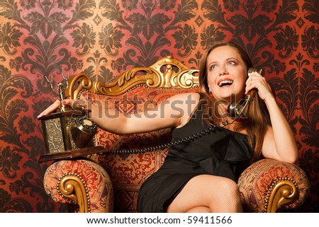 woman in black dress sitting on a vintage chair and talking on the old phone. looks up, bright emotions