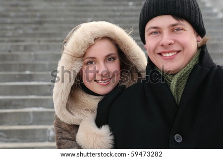 young girl in coat with hood embracing man from back and smiling, half body, winter day, stairs on background