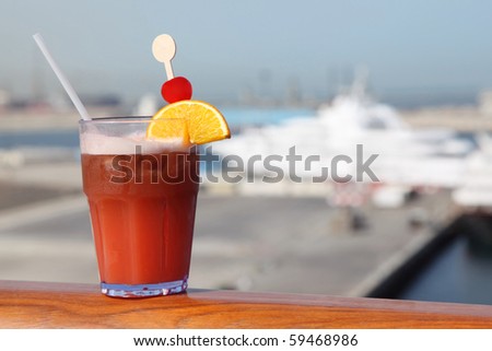 cocktail with fruits in glass on ship deck rail, port with cruise liner on background