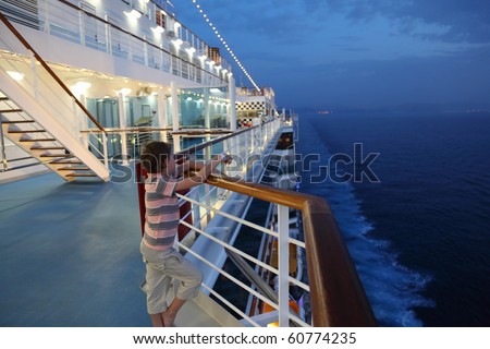 little boy wearing shorts and striped shirt standing on deck of a ship and looking away