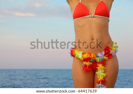 beautiful young woman dressed in bathing suit stands on beach. Hawaiian garland of flowers at the waist