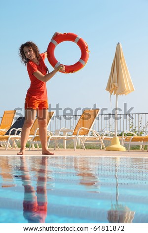 Beautiful young woman in shorts and T-shirt throws red buoy ring to pool