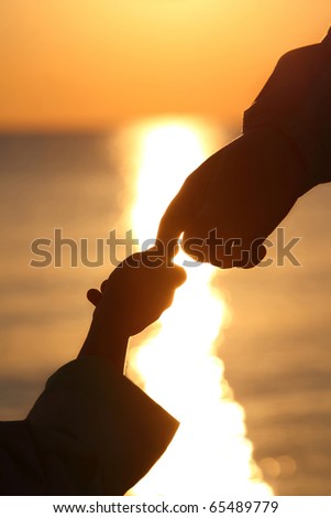 Silhouettes of child\'s and grown man hands which adjoin fingers in  evening ashore exterminating during sunset