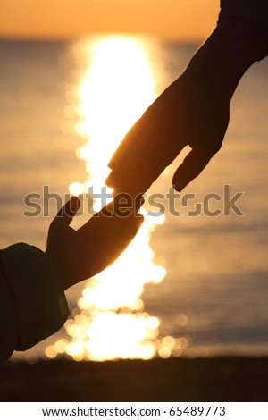 Silhouettes of two hands of child and  grown man adjoin fingers in evening at seaside during sunset