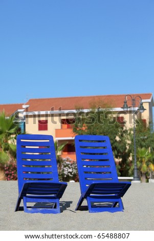Two blue plastic chairs stand under  sun on  beach near cottages