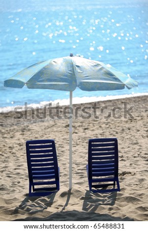 Ashore  in  day-time on sand two empty plastic chairs cost under  beach umbrella, shallow depth of focus
