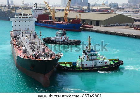 Two small boats docked to industrial ship in port at sunny day