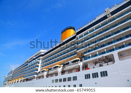Large cruise ship with yellow funnel and blue balcony rise to blue sky