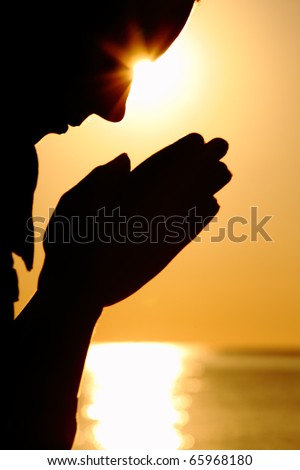 Silhouette of woman which sits near  sea opposite  sun and laid down hands before itself and prays
