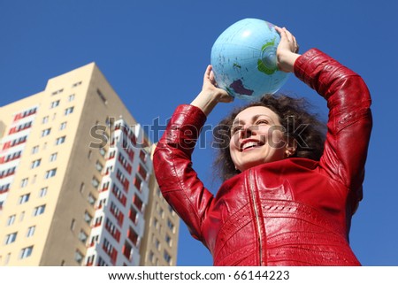 beautiful young woman in red jacket holding balloon in form of globe. multi-storey yellow house