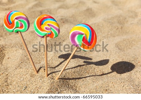 three multicolored lollipops sticked in sand on beach, sunny