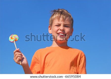little boy in orange shirt holding multicolored lollipop, blue sky