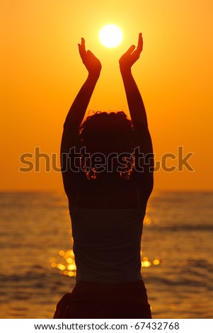 beautiful young woman standing on beach, watching sunset, holding  sun in hands