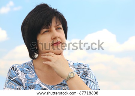 portrait of brunette plumpy mature serious woman, hand on chin, blue sky and clouds