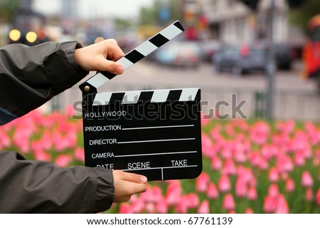 Cinema clapper board in the hands of boy on field with tulips on urban streets