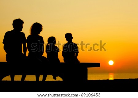 Father with mother and two children  sit on  bench on  beach in  evening and converse