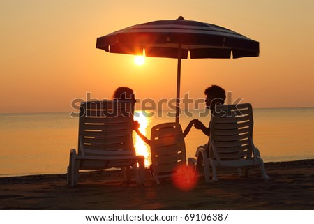 Mother with father and daughter sit on  beach on deck-chairs on sunset and to hold on to  hands