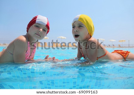 Two girls lie in  day-time in  pool opposite each other and speak