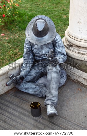 alive sculpture of cowboy sitting, ask for handout and keep revolvers