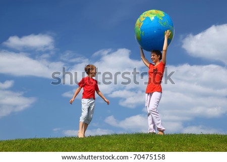 Mother stands on  grass and holds hands  large inflatable ball on  head,  boy comes running to it